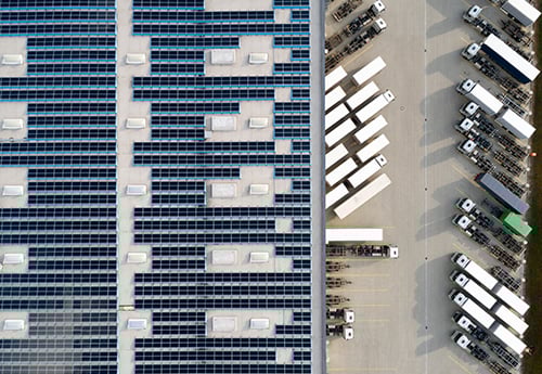 aerial view of freight trucks in the parking lot outside an industrial facility with solar panels on the roof
